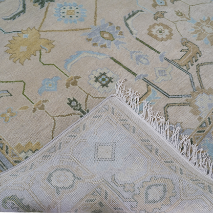 A close-up view of a handcrafted rug featuring floral patterns with pink undertones and avocado green accents, along with a detailed texture and fringed edge.