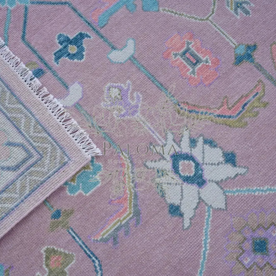 Close-up view of a handcrafted area rug with geometric and floral patterns in pink, blue, and multicolor.
