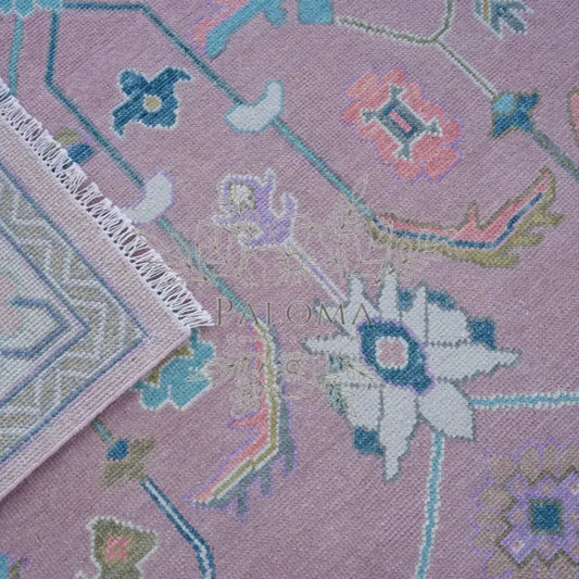 Close-up view of a handcrafted area rug with geometric and floral patterns in pink, blue, and multicolor.
