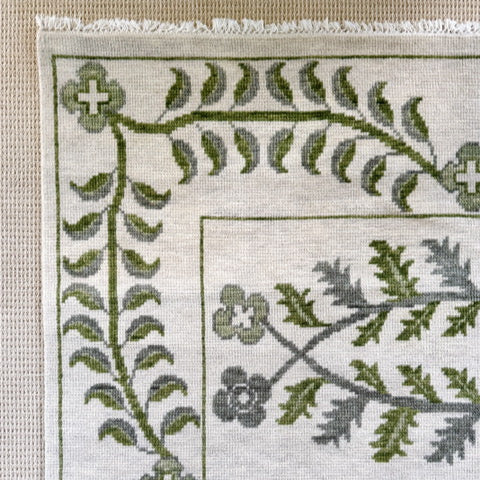 Close-up of a cross-stitched pattern with green leaves and flowers on a white fabric background.