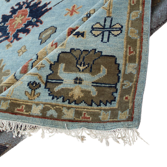A close-up view of a handmade rug featuring geometric and traditional patterns with sky blue, moss green, and navy colors.