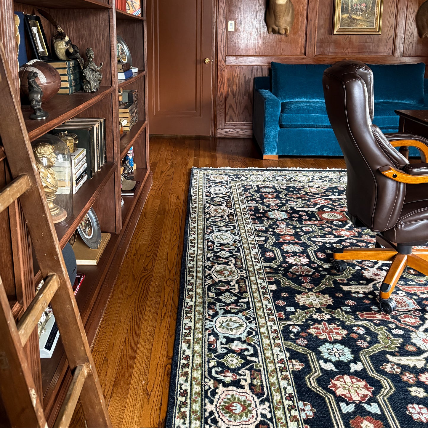 Navy floral Oushak rug styled beside a brown leather chair
