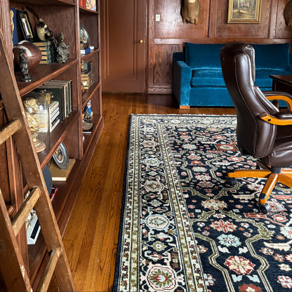 Navy floral Oushak rug styled beside a brown leather chair